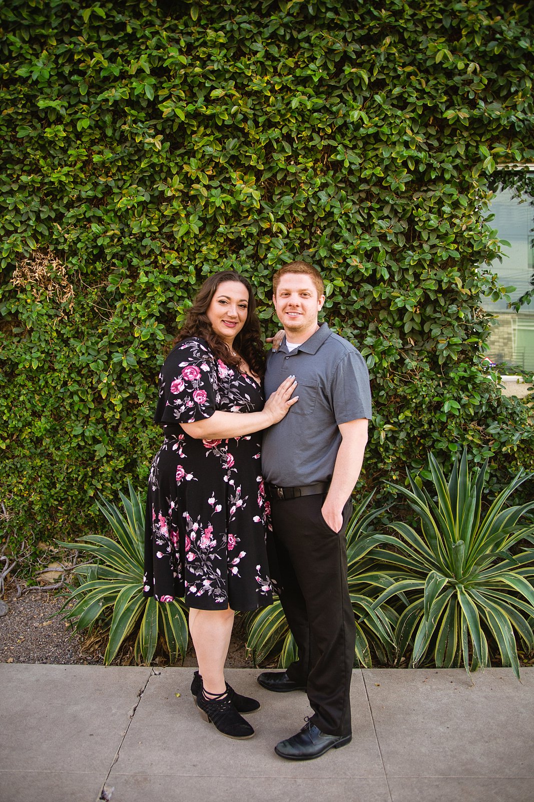 Couple posing in front of living plant wall during their downtown Phoenix engagement session by PMA Photography.