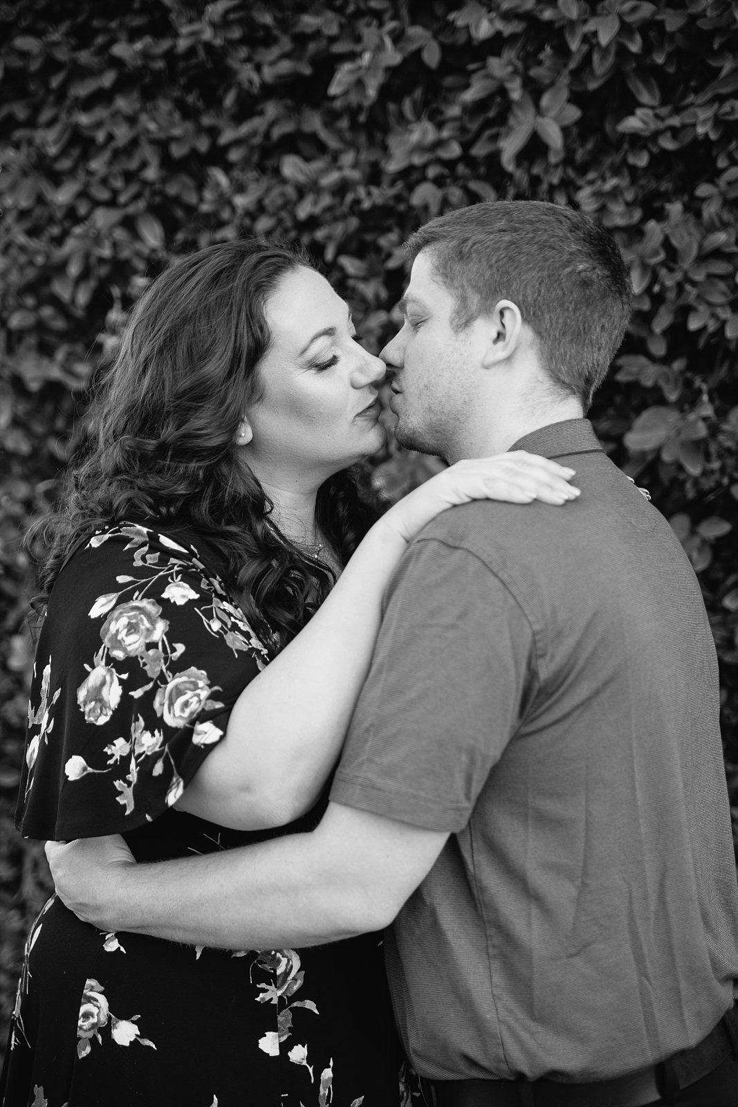 Black and white photograph of couple sharing an intimate moment in front of living plant wall during their downtown Phoenix engagement session by PMA Photography.