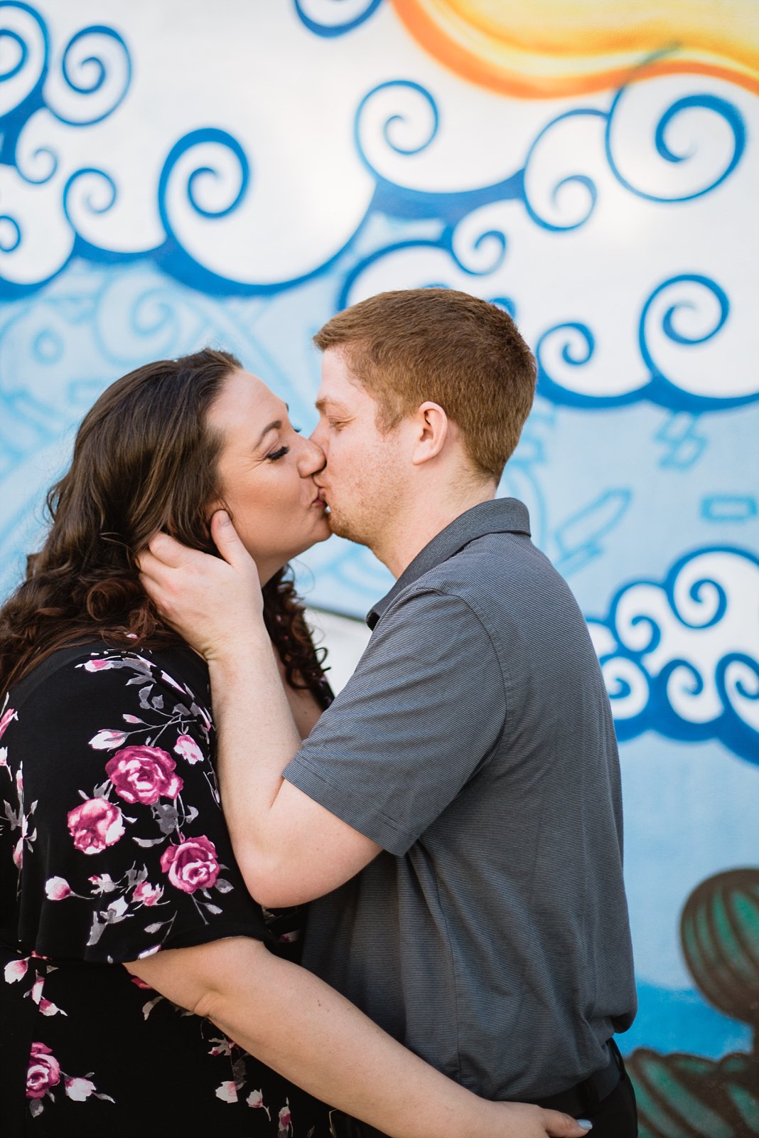 Couple kissing in front of art mural during their Roosevelt Row Art District engagement session by PMA Photography.