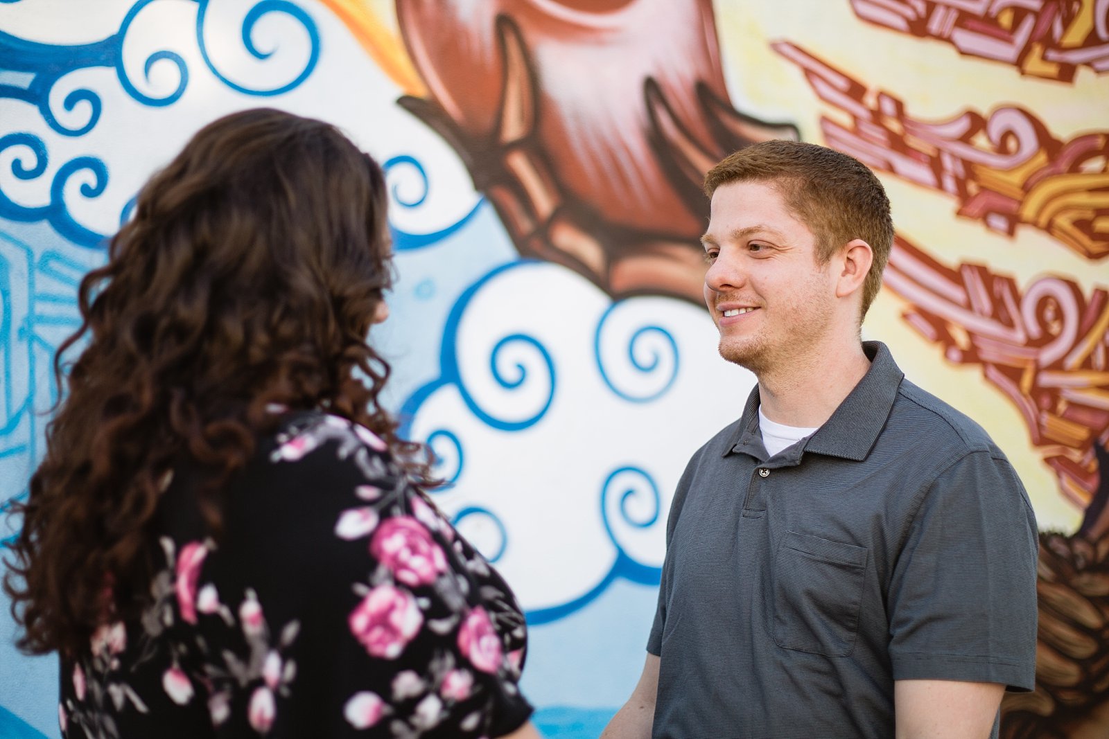 Couple looking at each other in front of art mural during their Roosevelt Row Art District engagement session by PMA Photography.