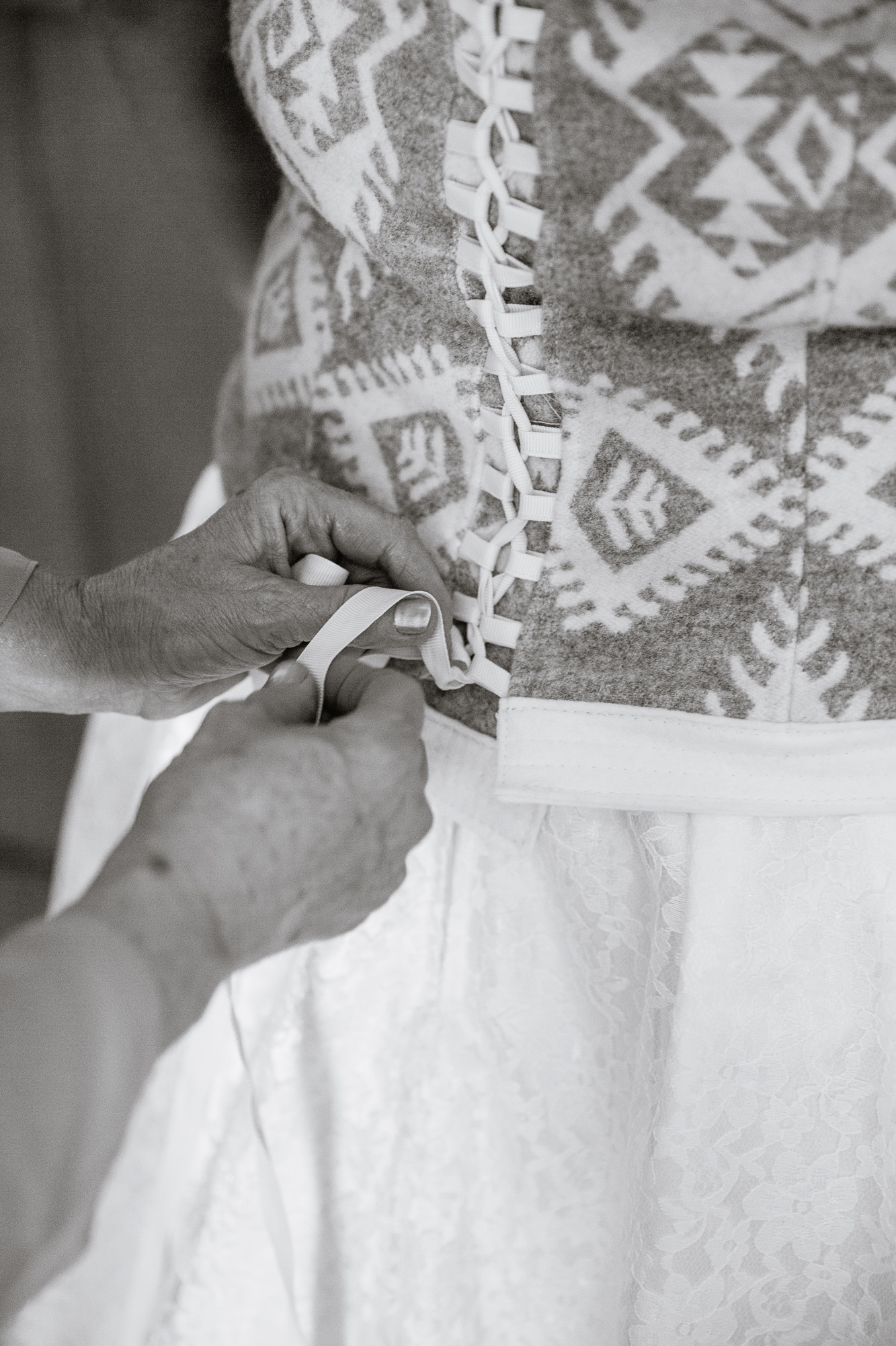 Black and white image of the bride's mother tying her wedding dress by PMA Photography.