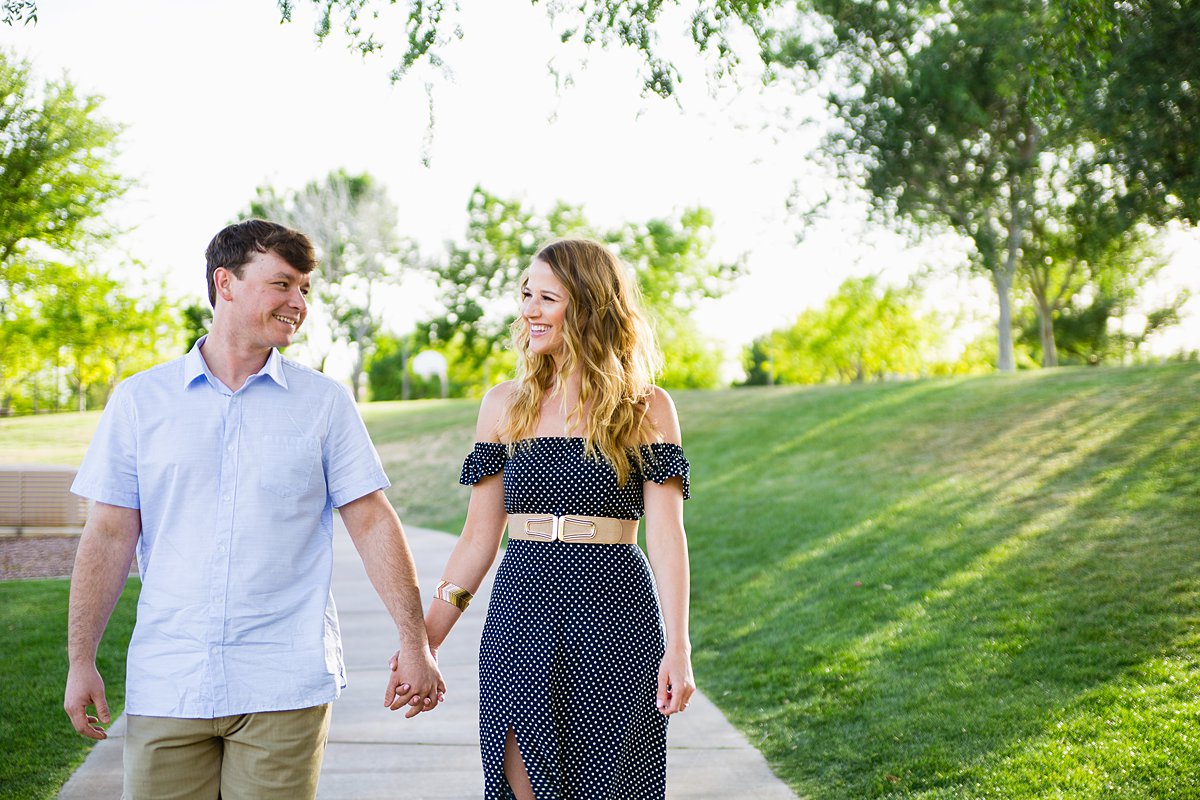 Couple holding hands and walking through Anthem Community Park by engagement photographer PMA Photography.