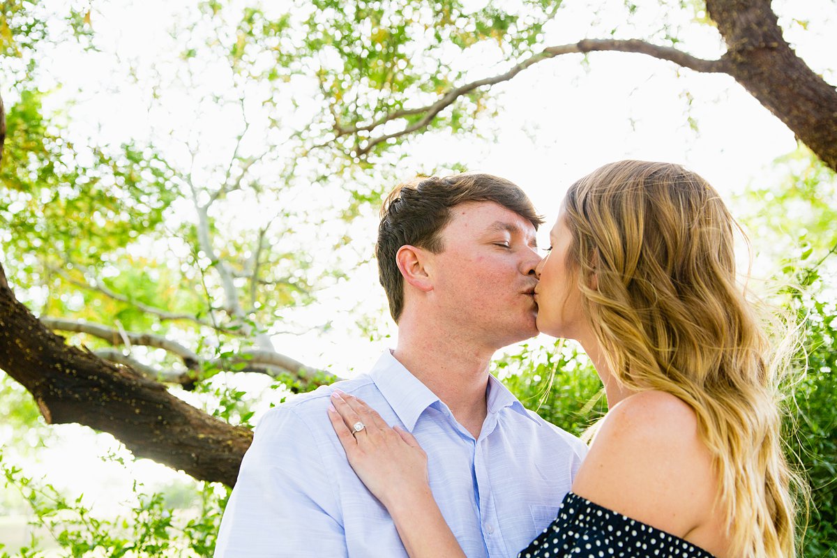 Couple kissing in front of a palo verde tree during their engagement session by PMA Photography.