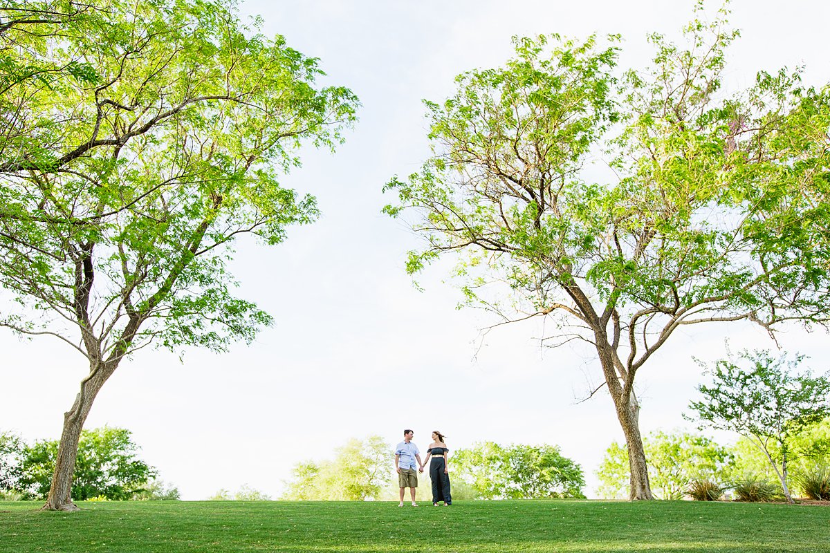 Couple holding hands between trees at their engagement session by PMA Photography.