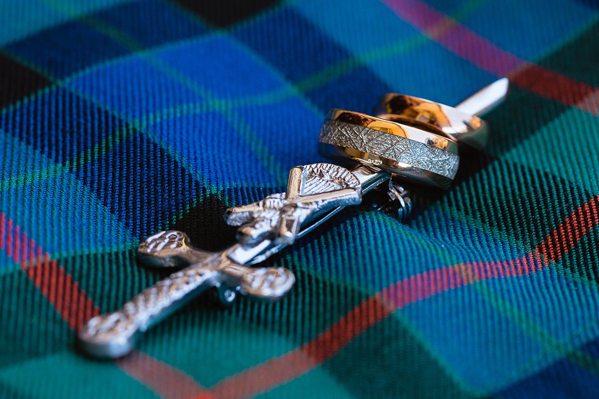 Wedding rings on a sword pin on a kilt for a Scottish inspired wedding by PMA Photography.