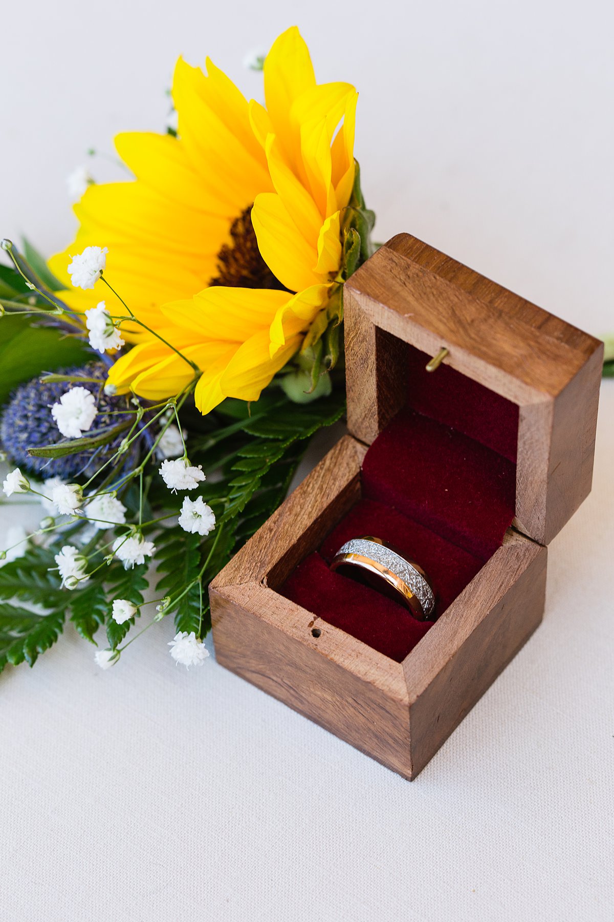 Unique gold wedding band in wooden box with sunflower boutonniere by PMA Photography.