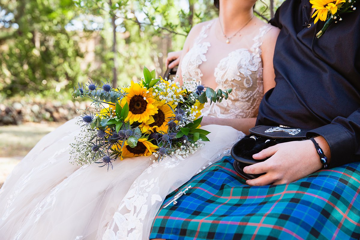 Bride lace and nude dress and grooms kilt as they sit together with her sunflower bouquet by PMA Photography.