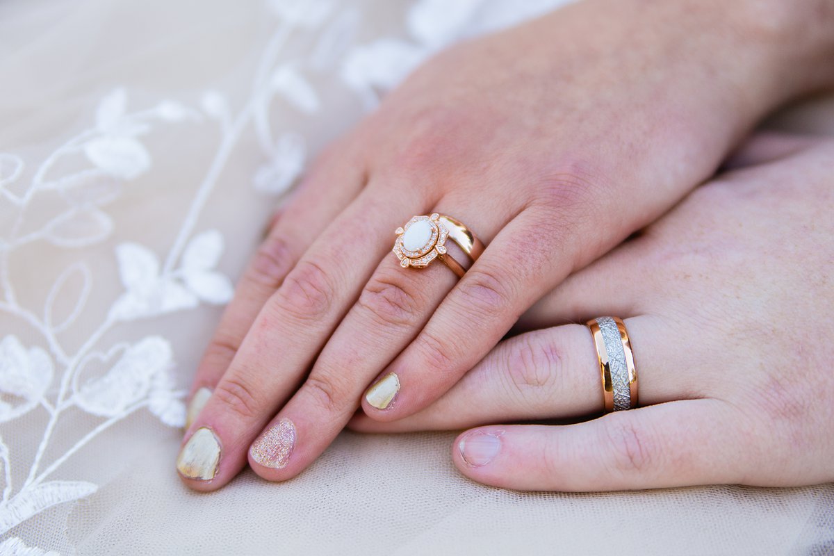 Bride and groom's unique rose gold, opal, and white wedding bands by PMA Photography.