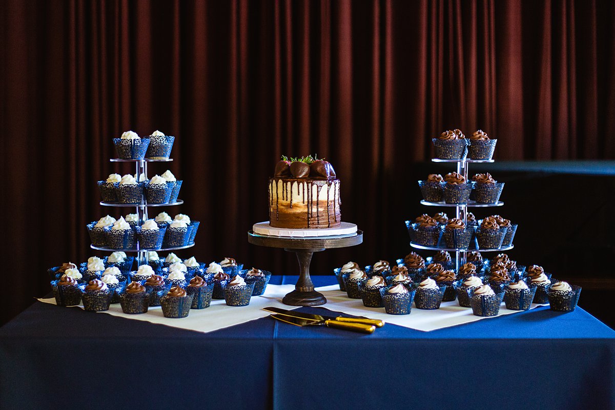 Strawberry and chocolate simple drip wedding cake surrounded by cupcakes by PMA Photography.