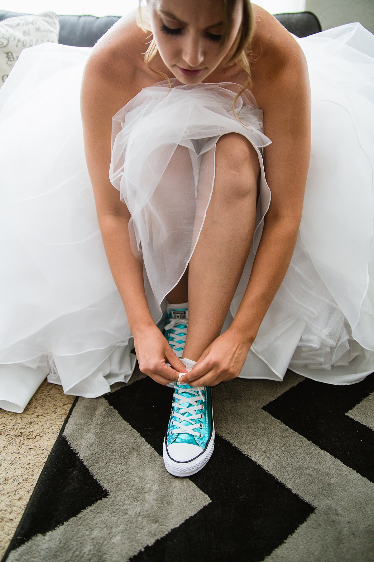 Bride putting on her metallic turquoise converse in her wedding dress by Arizona wedding photographer PMA Photography.