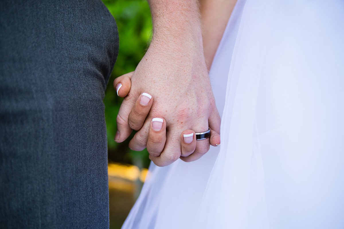 Close up image of the groom's black and silver wedding band while holding his bride's hand by Arizona wedding photographer PMA Photography.