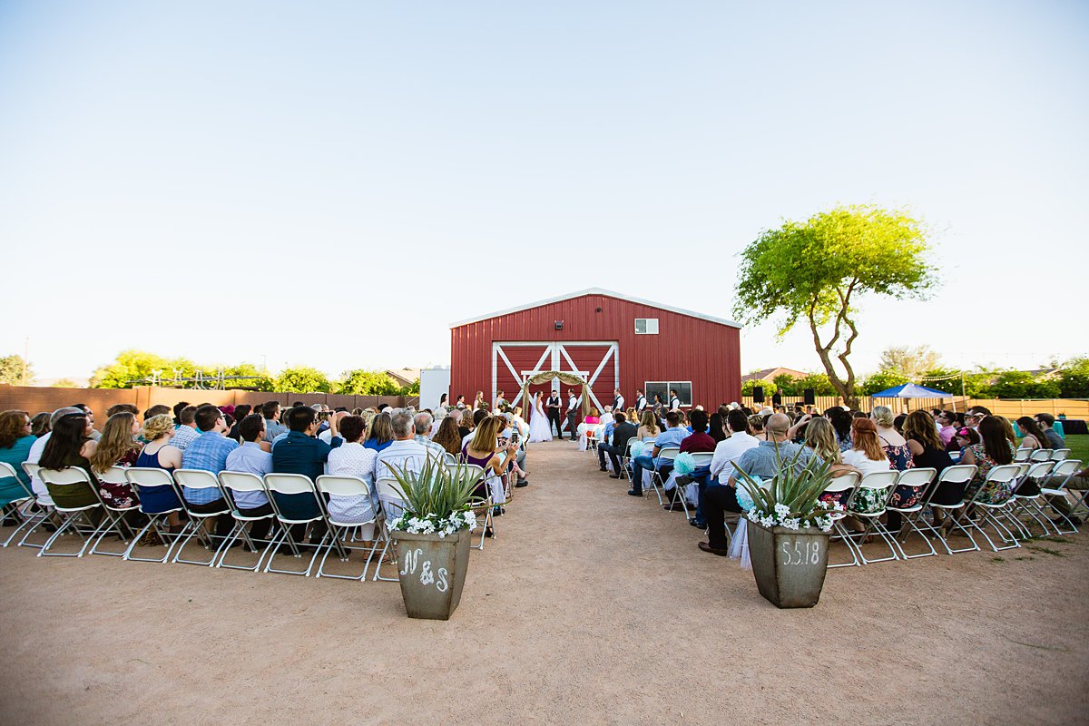 Backyard wedding ceremony in front of red barn by Arizona wedding photographers PMA Photography.