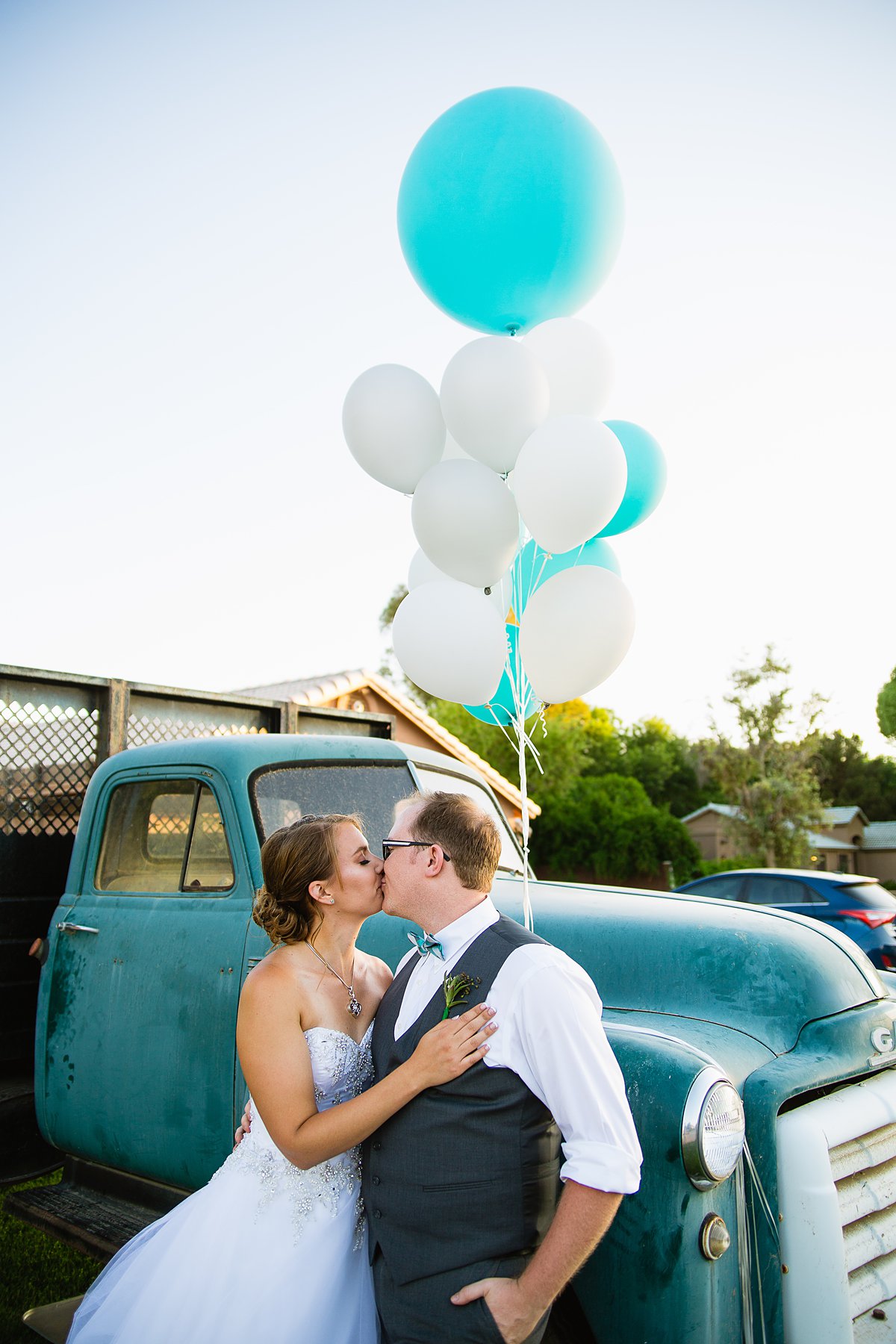 Bride and groom share a kiss in front of a vintage truck and balloons by Arizona wedding photographer PMA Photography.