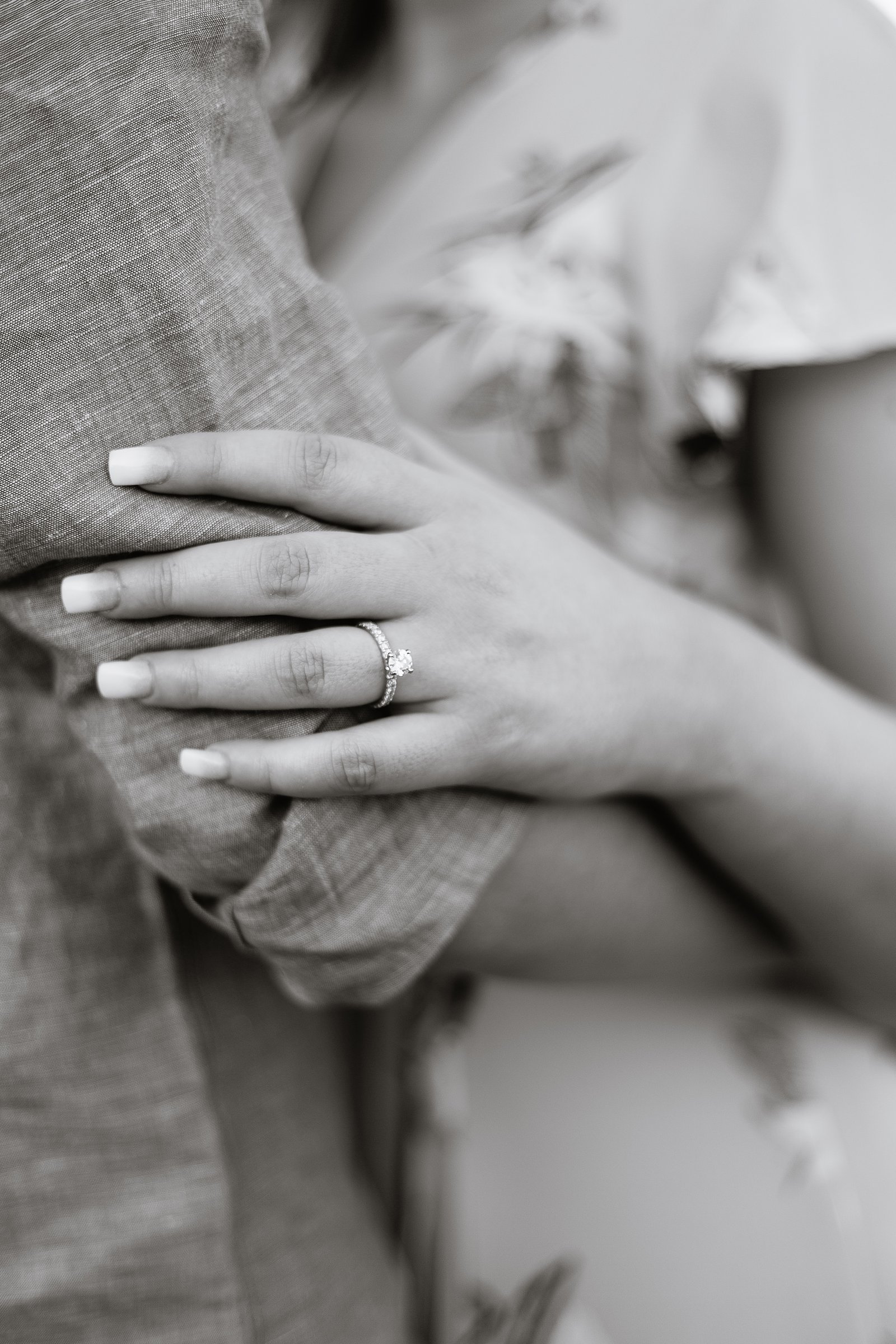 Black and white detail image of bride's engagement ring while holding her groom's arm by PMA Photography.