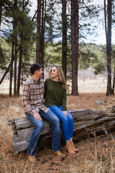 Couple looking at each other while sitting on a log during their Flagstaff engagement session by photographer PMA Photography.