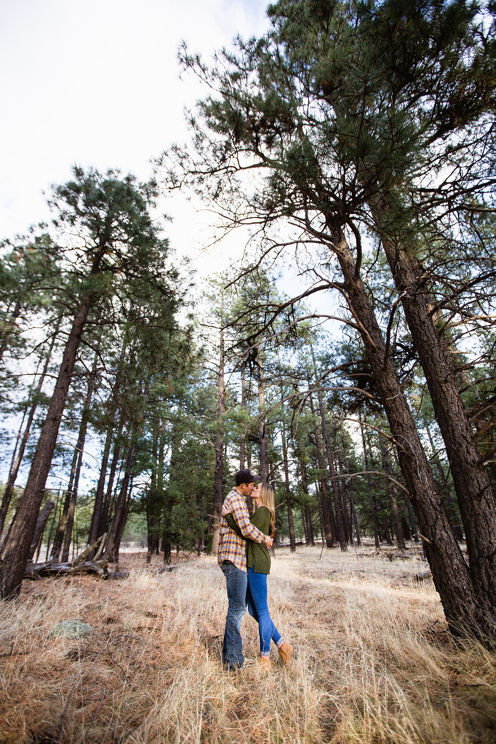 Couple share a kiss in the woods during their Flagstaff engagement session by PMA Photography.