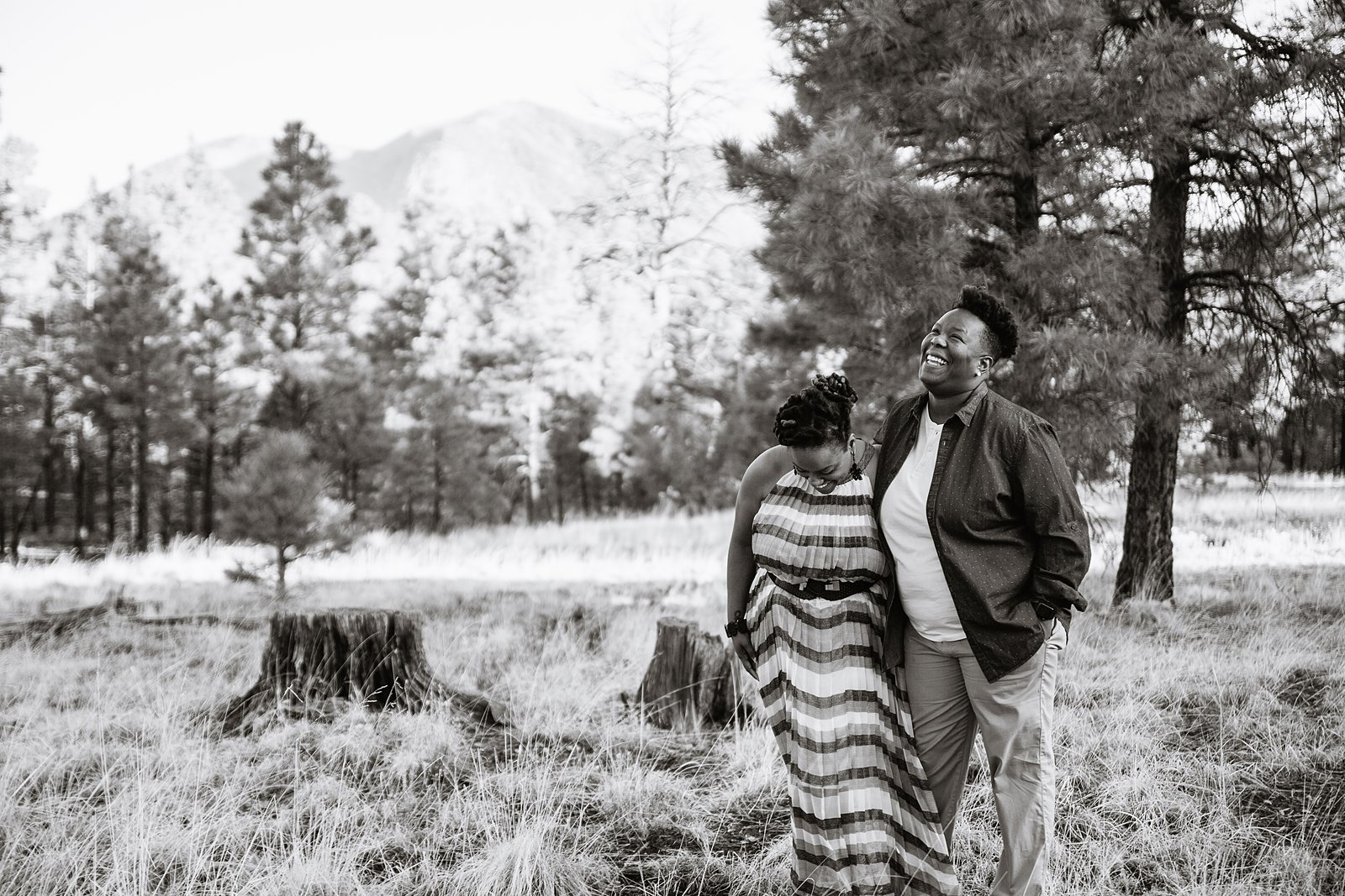 Same sex couple laugh together in the forest during their Flagstaff engagement session by Arizona engagement photographer PMA Photography.