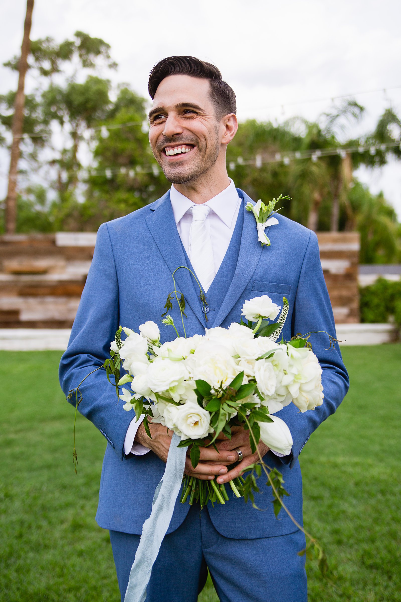 Groom laughing while holding a white garden inspired bouquet by PMA Photography.