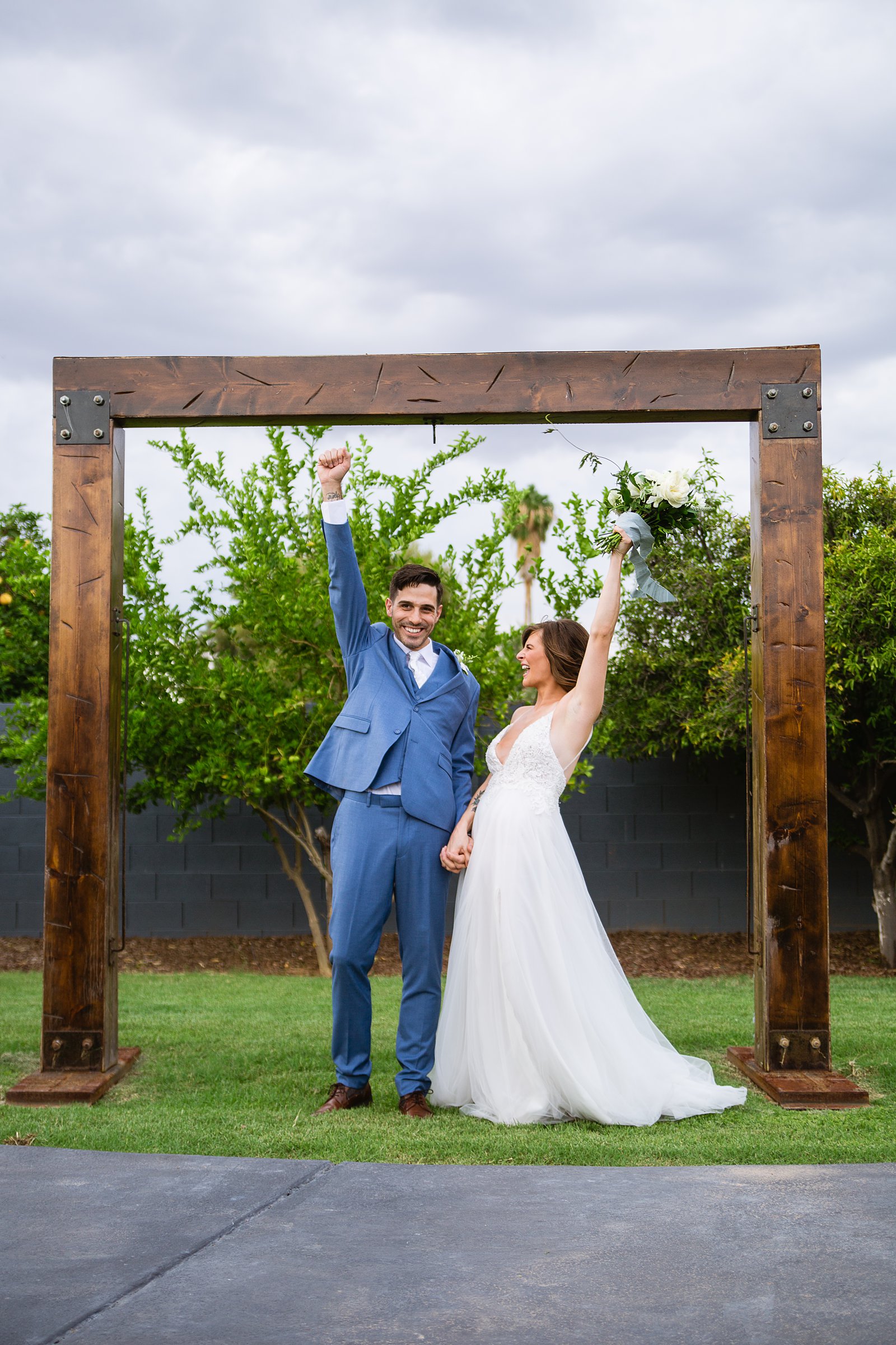 Bride and groom cheer under a rustic alter at Gather Estate wedding venue by Arizona wedding photographer PMA Photography.