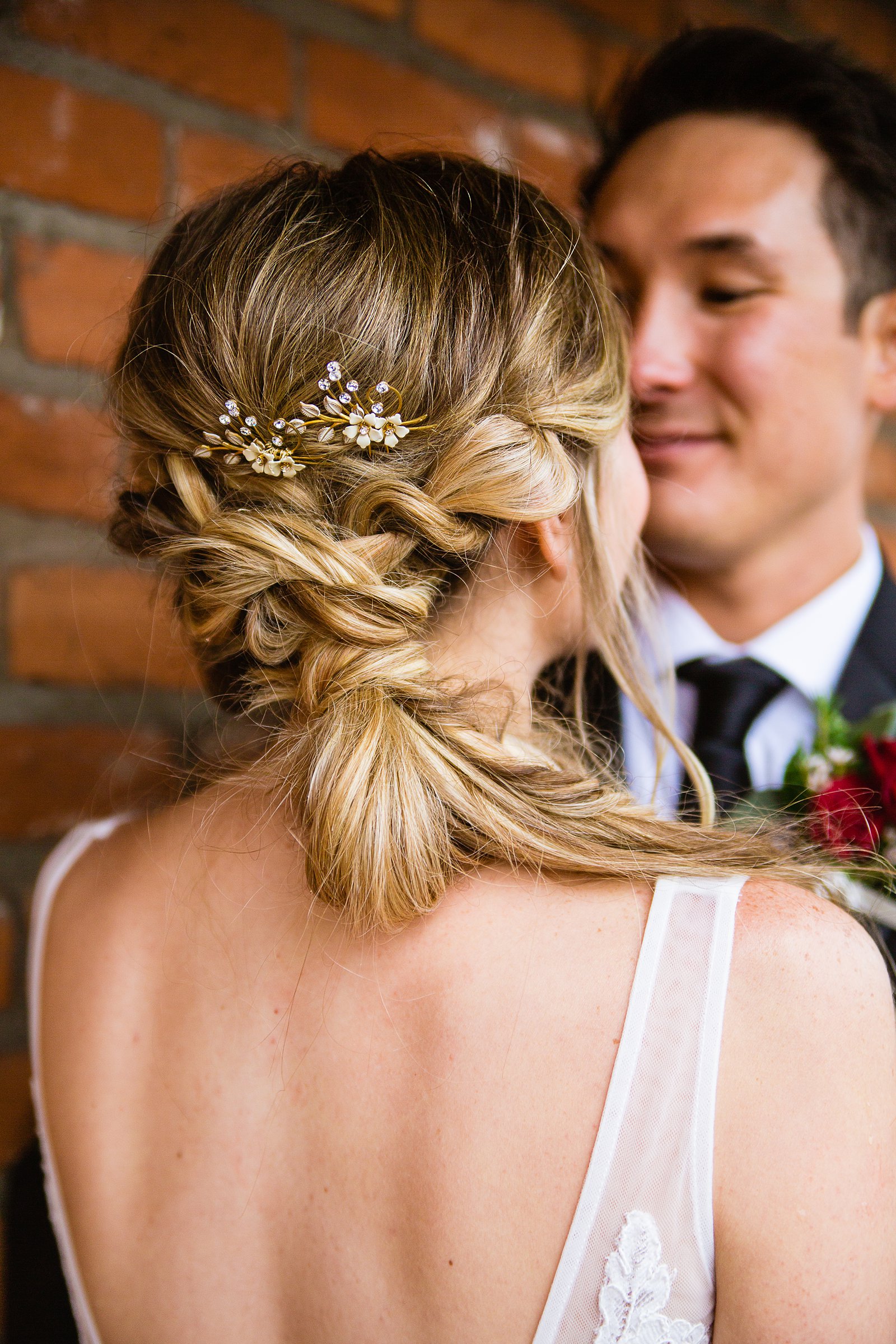 Bride's hair clip and braided hair on her wedding day while looking at her groom by PMA Photography.
