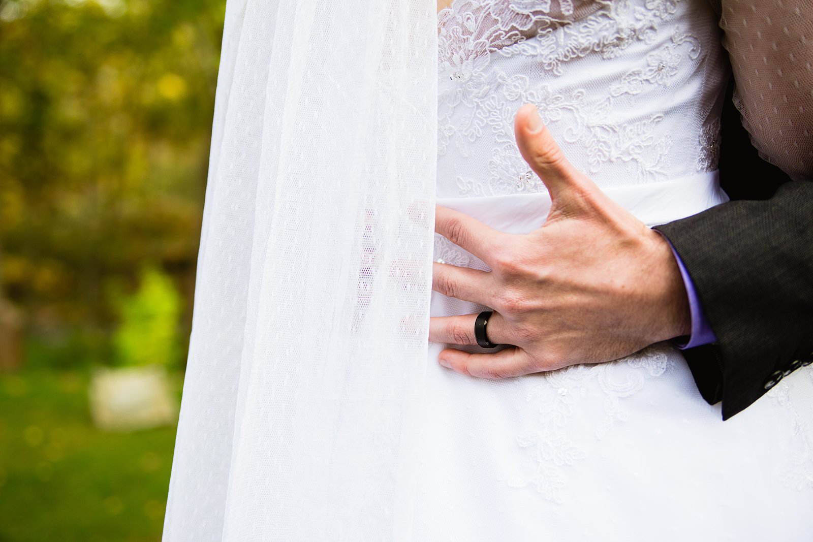 Grooms wedding band as he holds his bride by PMA Photography.