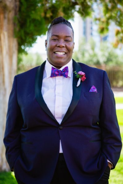 LGBT bride in a purple tux jacket and floral bow tie by Arizona wedding photographer PMA Photography.