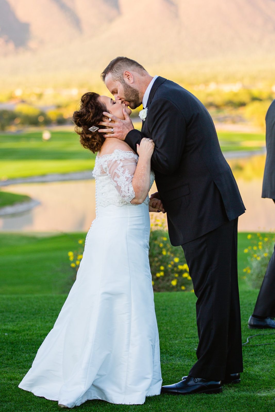 Bride and groom share their first kiss during their wedding ceremony at Superstition Mountain Clubhouse by Arizona wedding photographer PMA Photography.