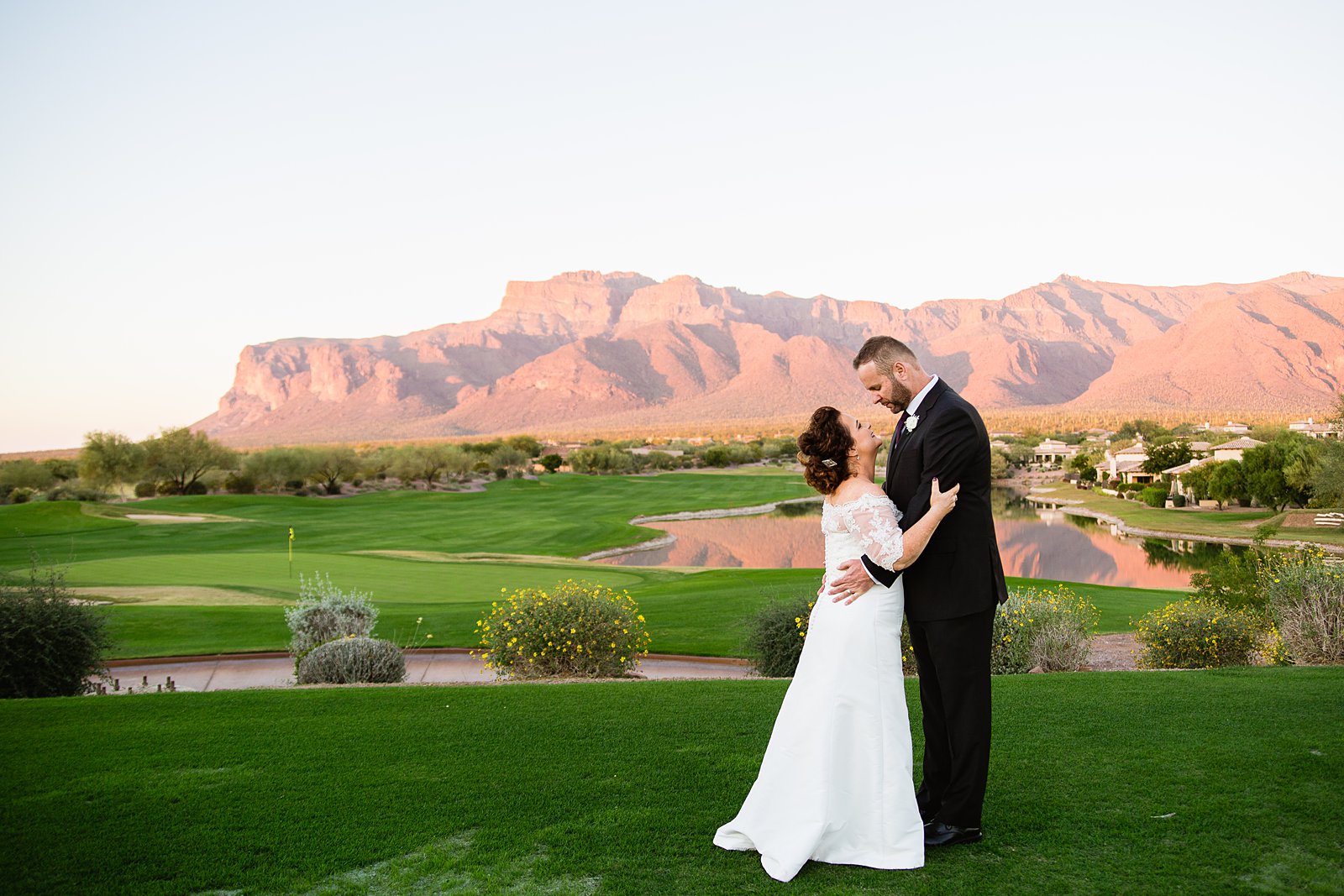 Bride and groom share an intimate moment as the sun sets on the Superstition Mountains at their Superstition Mountain Clubhouse wedding by Arizona wedding photographer PMA Photography.