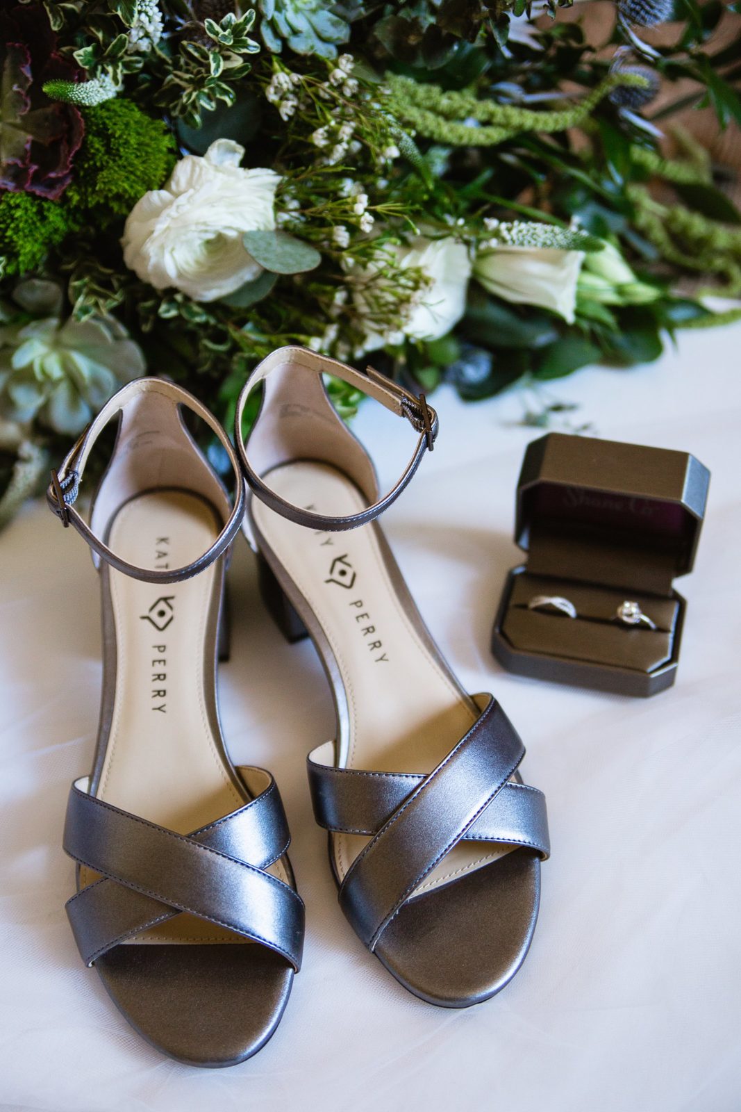 Brides's wedding day details of silver shoes, garden bouquet, and wedding band by PMA Photography.