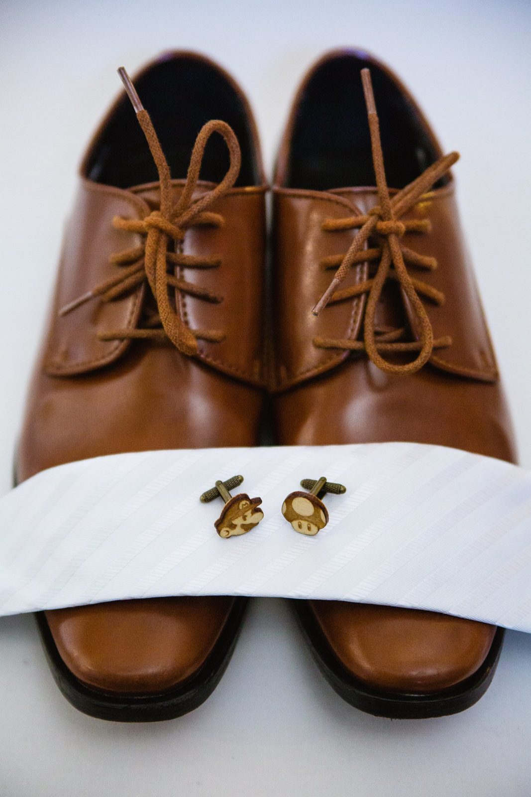 Groom's wedding day details of tan shoes, white tie, and wooden Mario Bros cuff links by PMA Photography.