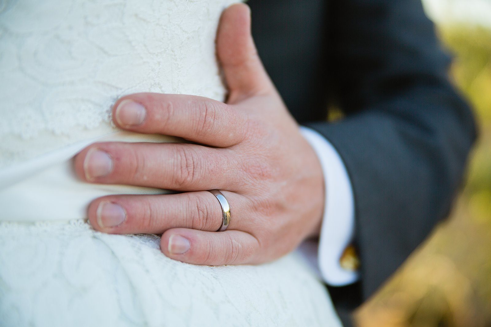 Groom's simple white gold wedding band as he holds his wife by PMA Photography.
