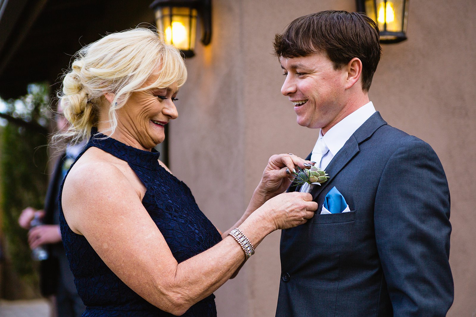 Mother of the groom pinning a succulent boutonniere on the groom while getting ready for his wedding by PMA Photography.