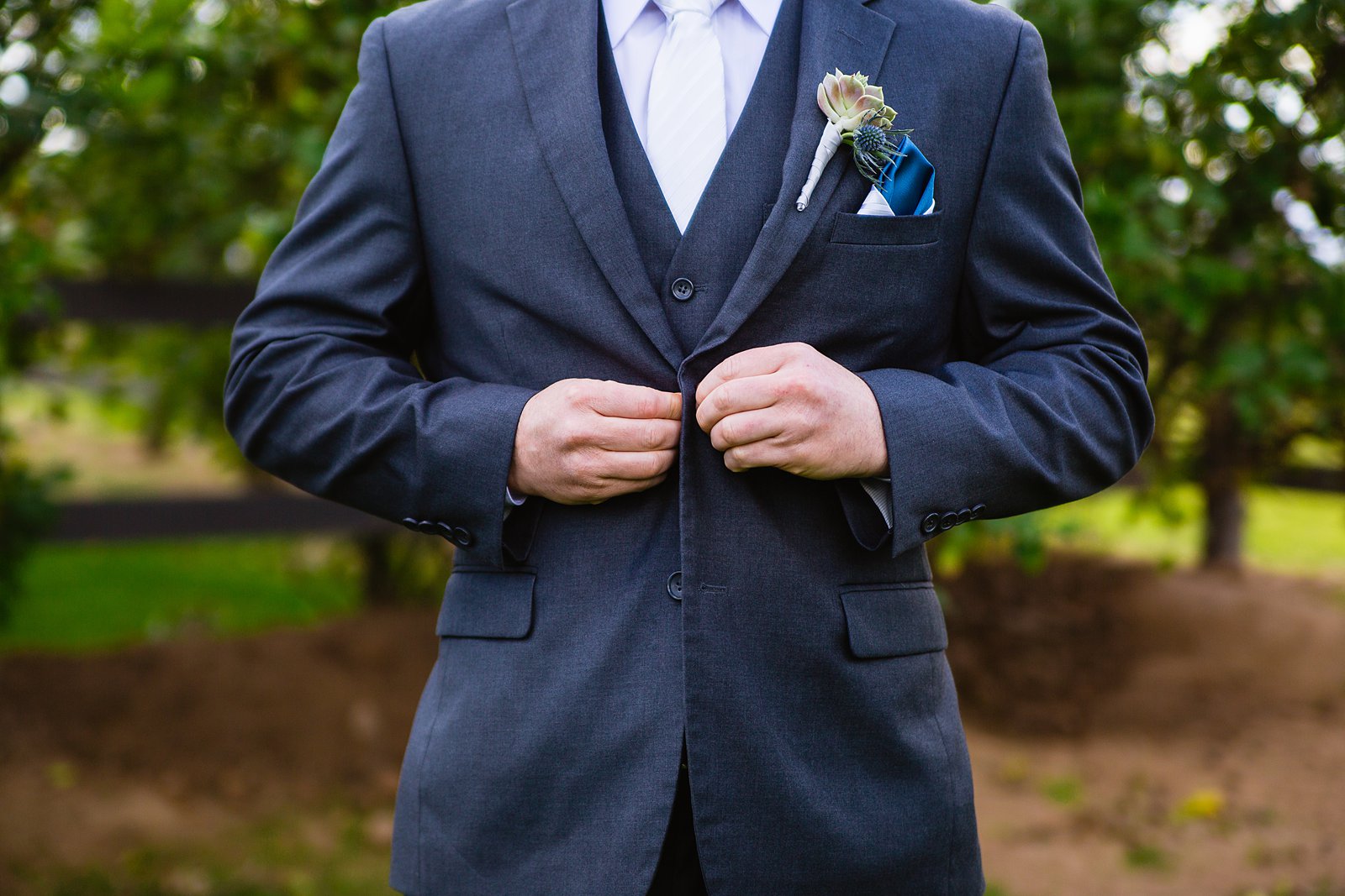 Groom buttoning up his grey suit jacket while getting ready for his wedding day by Arizona wedding photographer PMA Photography.