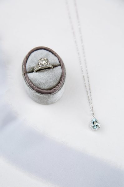 Brides's wedding day details of a blue necklace and square white gold wedding ring and band set by PMA Photography.