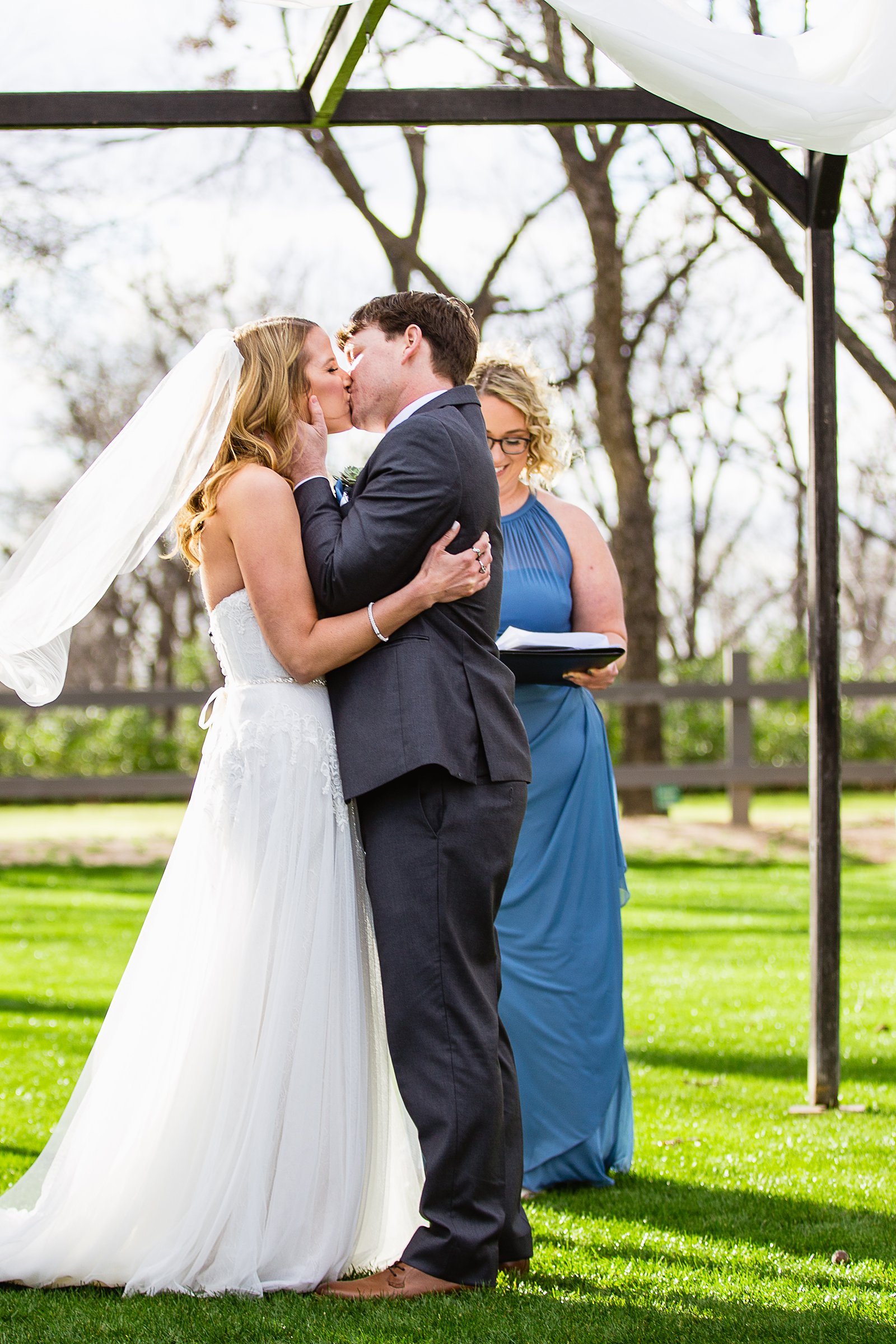 Bride and Groom share their first kiss during their wedding ceremony at Venue At The Grove by Arizona wedding photographer PMA Photography.