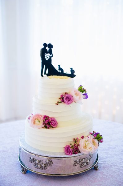 Simple wedding cake with pink and purple flowers with custom cake topper of bride and groom with their cats by Arizona wedding photographer PMA Photography.