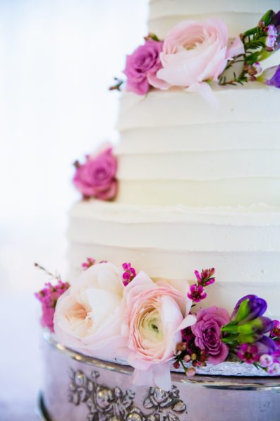 Simple wedding cake with pink and purple flowers by Arizona wedding photographer PMA Photography.
