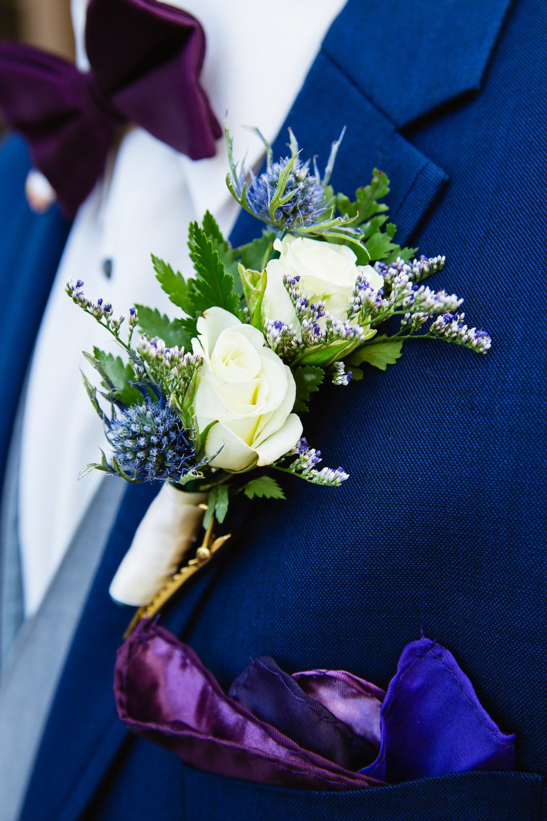White rose and blue thistle groom boutonniere on a navy suit lapel by PMA Photography.