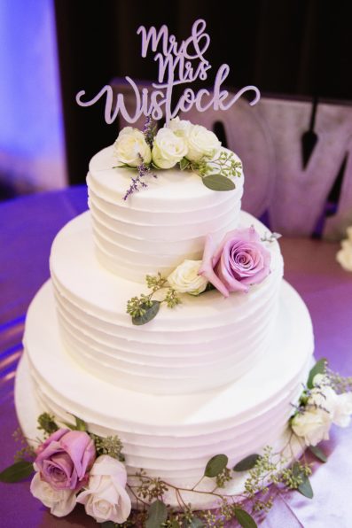 White and purple roses with eucalyptus decorating a simple white wedding cake by PMA Photography.