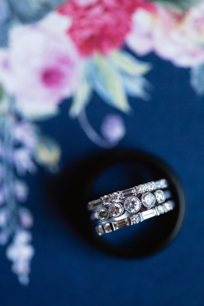 Bride's unique stacking wedding bands in her groom's black wedding band on their navy and floral wedding stationary by PMA Photography.