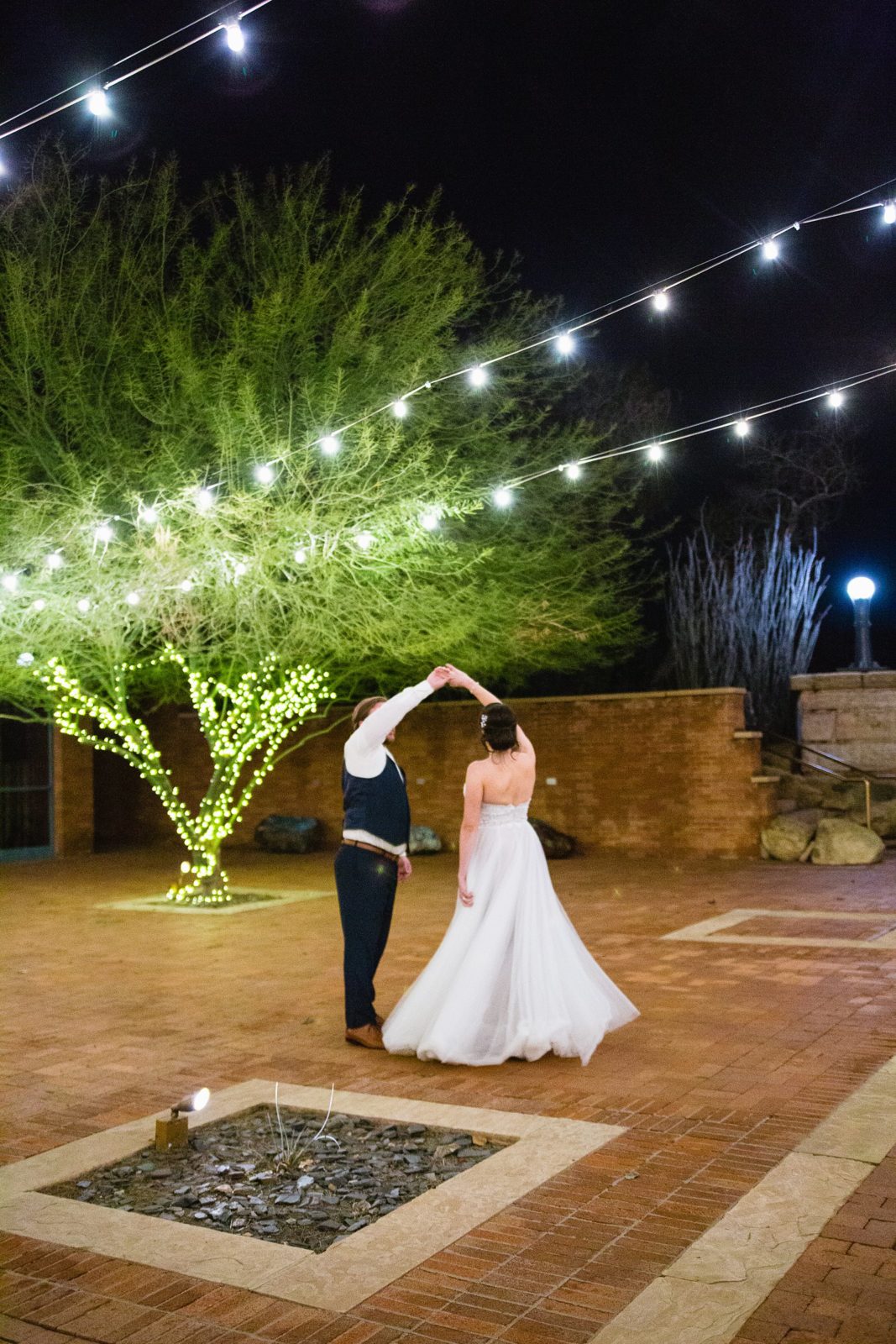 Bride and groom dancing under bistro lights at their wedding reception by Arizona wedding photographer PMA Photography.