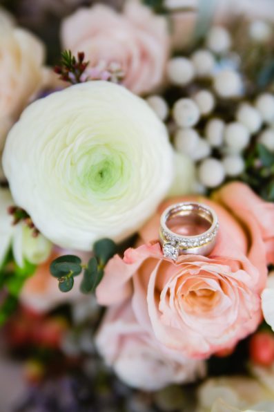 Classic white gold wedding rings on pink and white bridal bouquet flowers by PMA Photography.