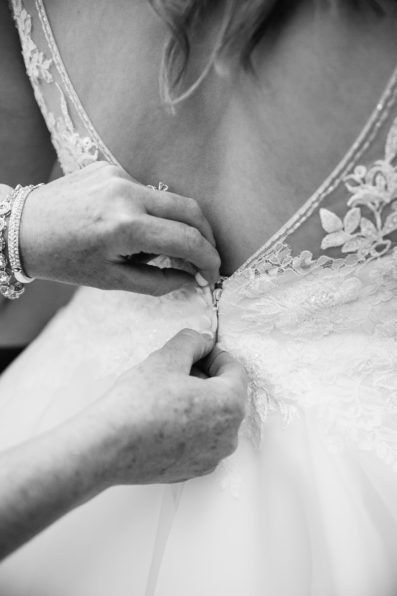 Bride's mother buttoning her lace wedding dress by PMA Photography.