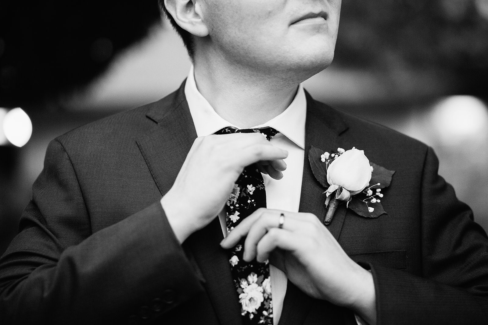 Groom adjusting his floral tie on his wedding day by PMA Photography.