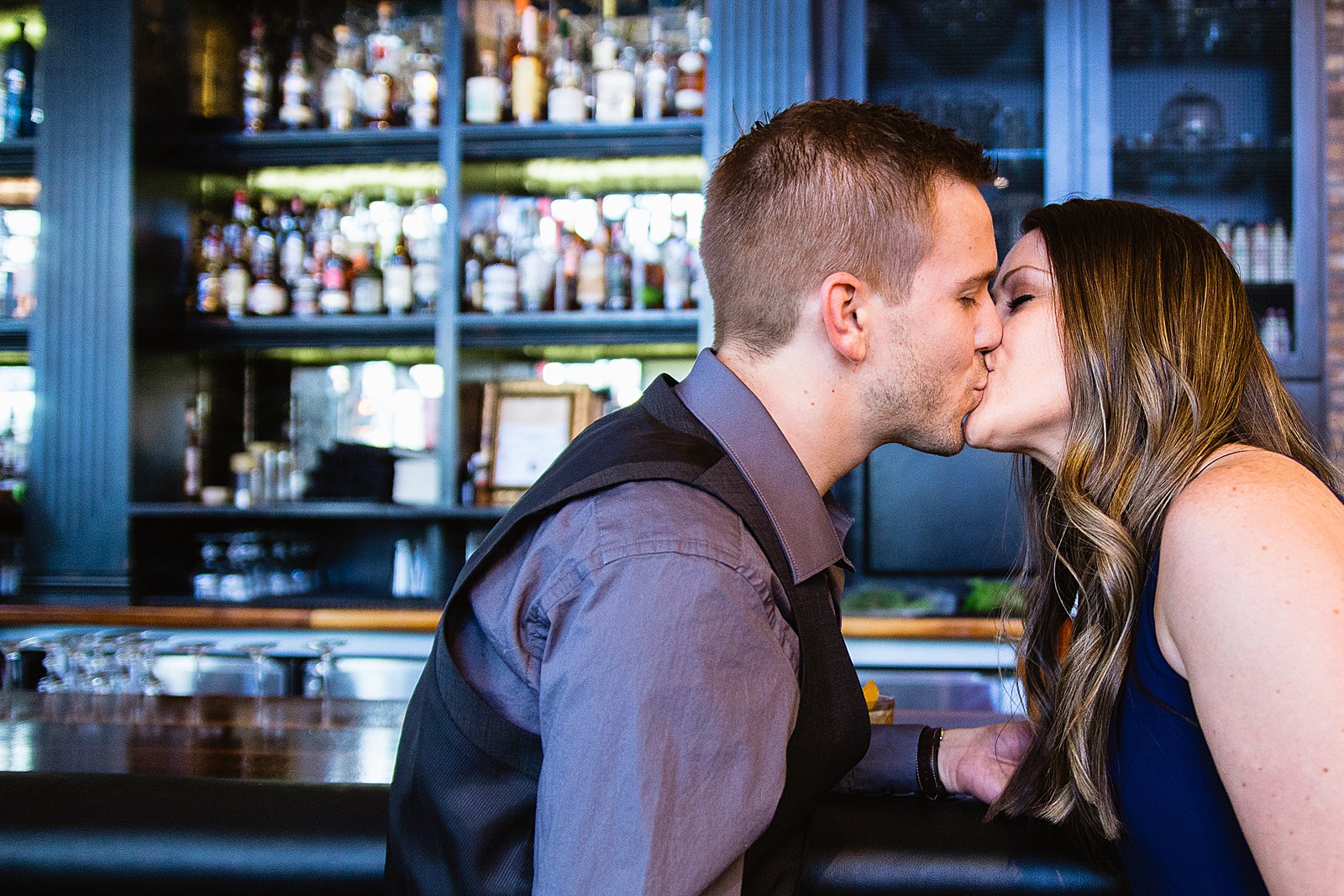 Couple share a kiss during their Downtown Phoenix bar engagement session by Phoenix wedding photographer PMA Photography.