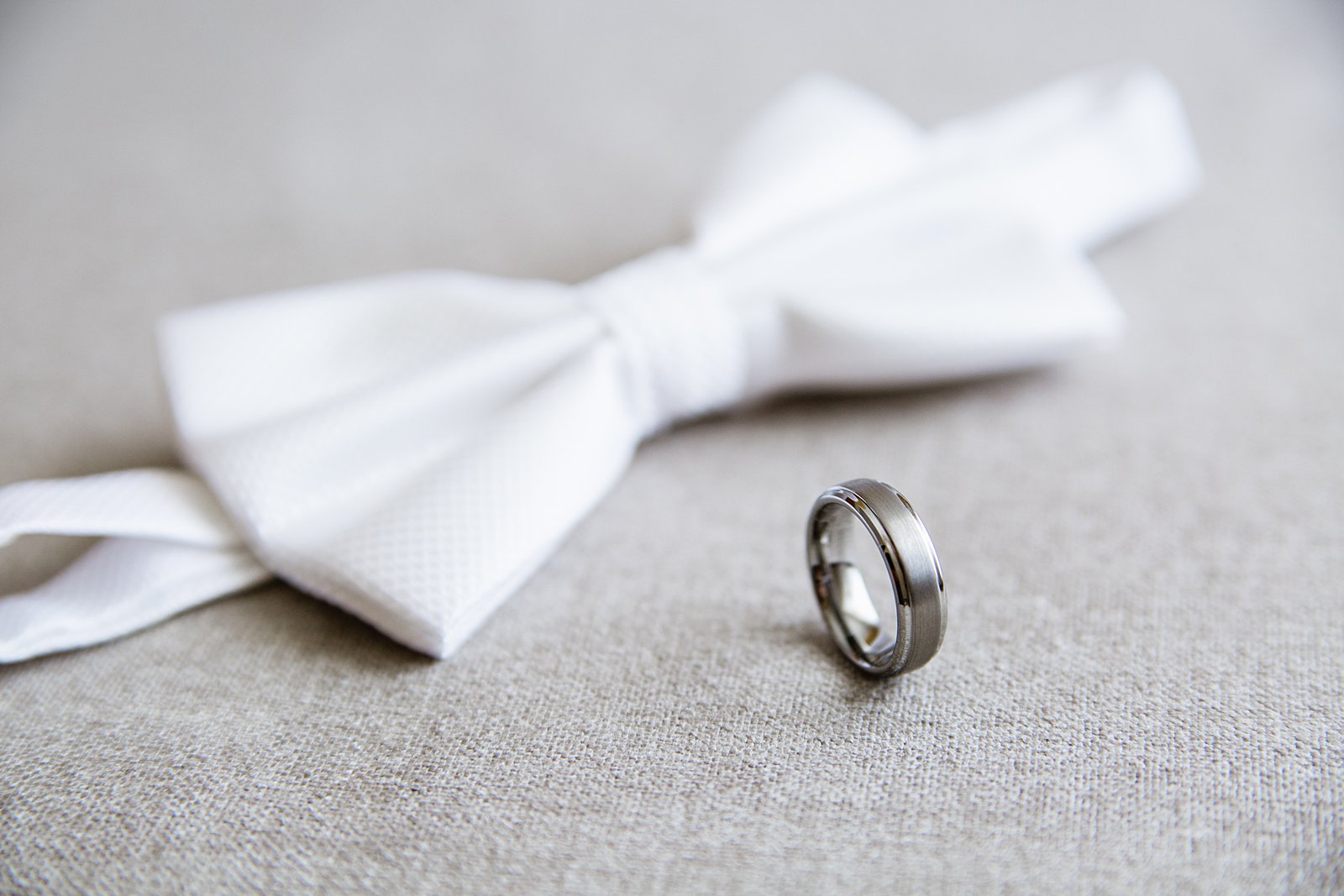 Groom's wedding day details of a wedding band and white bowtie by PMA Photography.