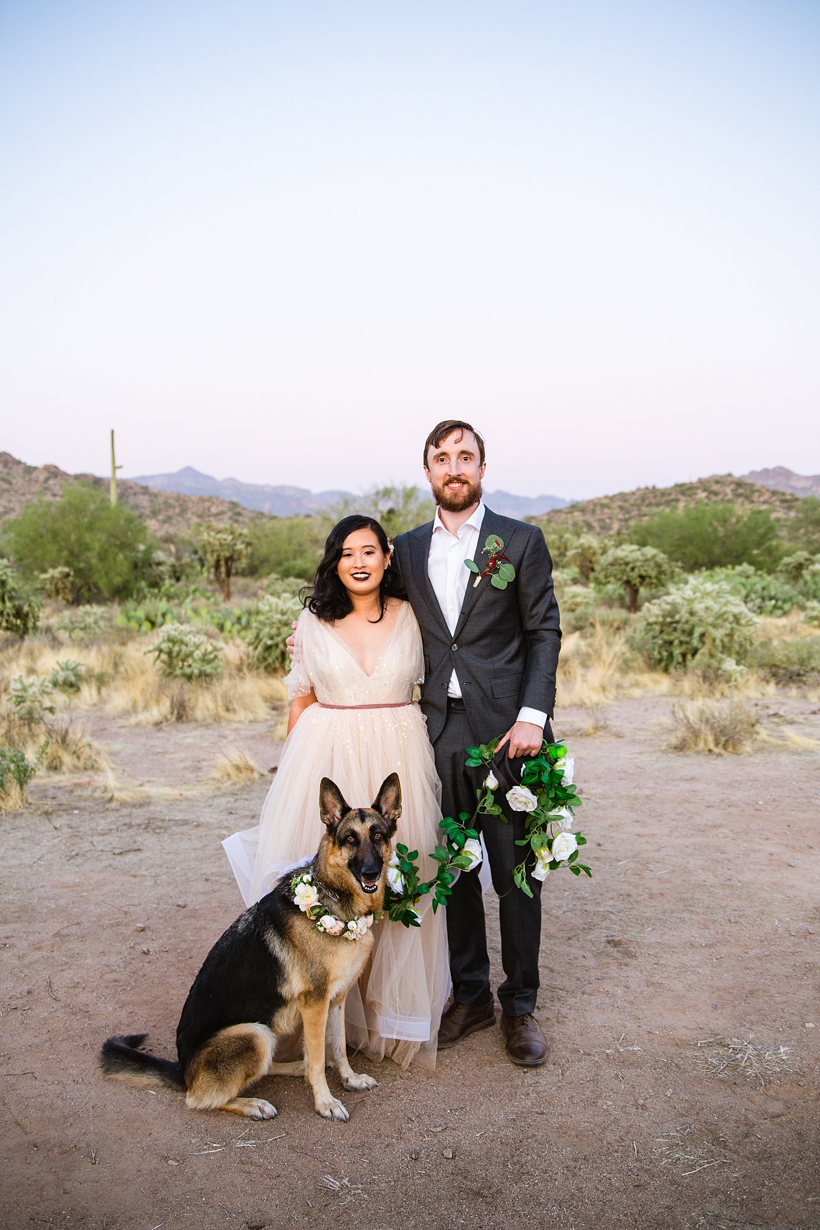 Bride and groom pose with their dog at a romantic desert wedding by PMA Photography.