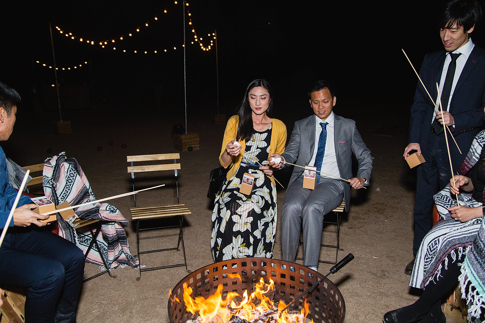 Guests roasting s'mores around a fire at a Cloth and Flame wedding reception by Phoenix wedding photographer PMA Photography.