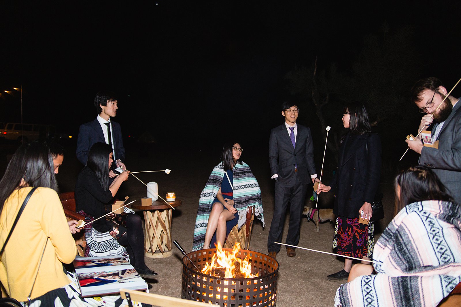 Guests roasting s'mores around a fire at a Cloth and Flame wedding reception by Phoenix wedding photographer PMA Photography.