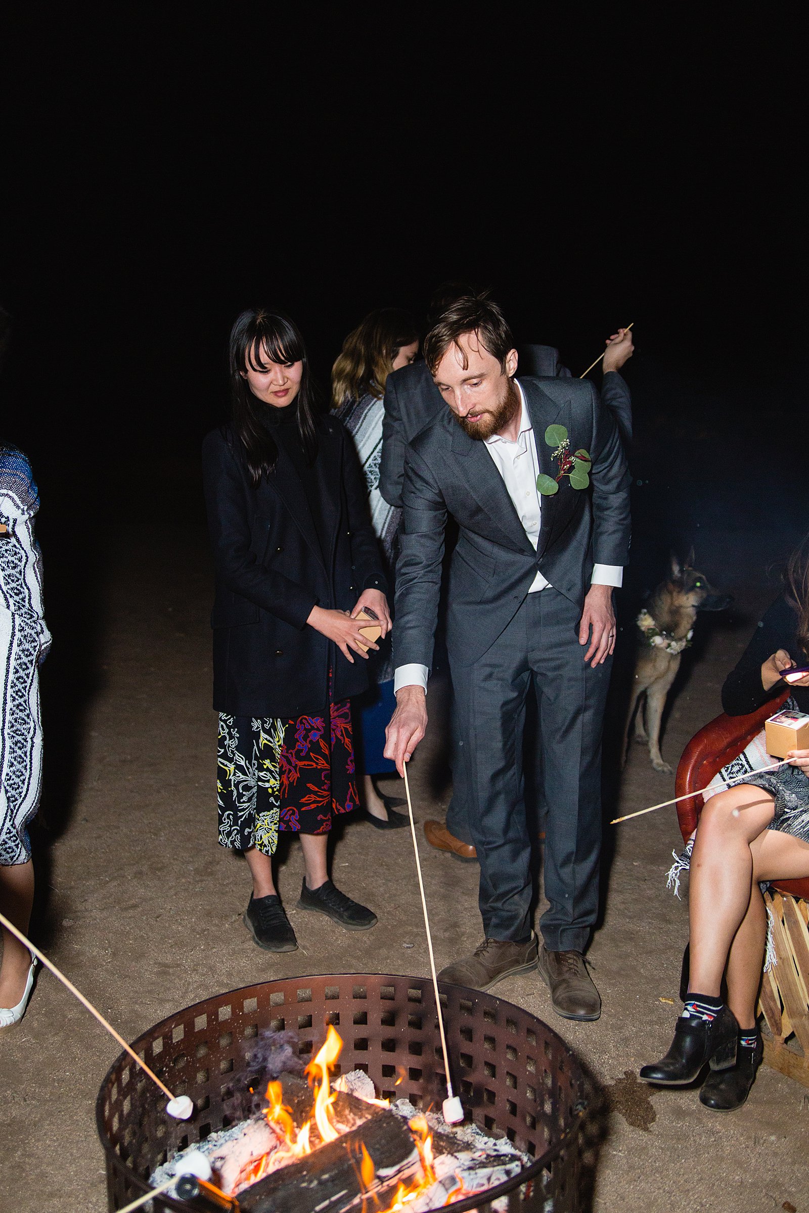 Groom roasting s'mores with guests at a Cloth and Flame wedding reception by Phoenix wedding photographer PMA Photography.